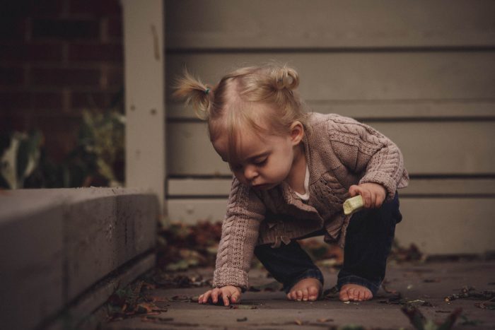 baby girl barefoot picking leaves up off the ground