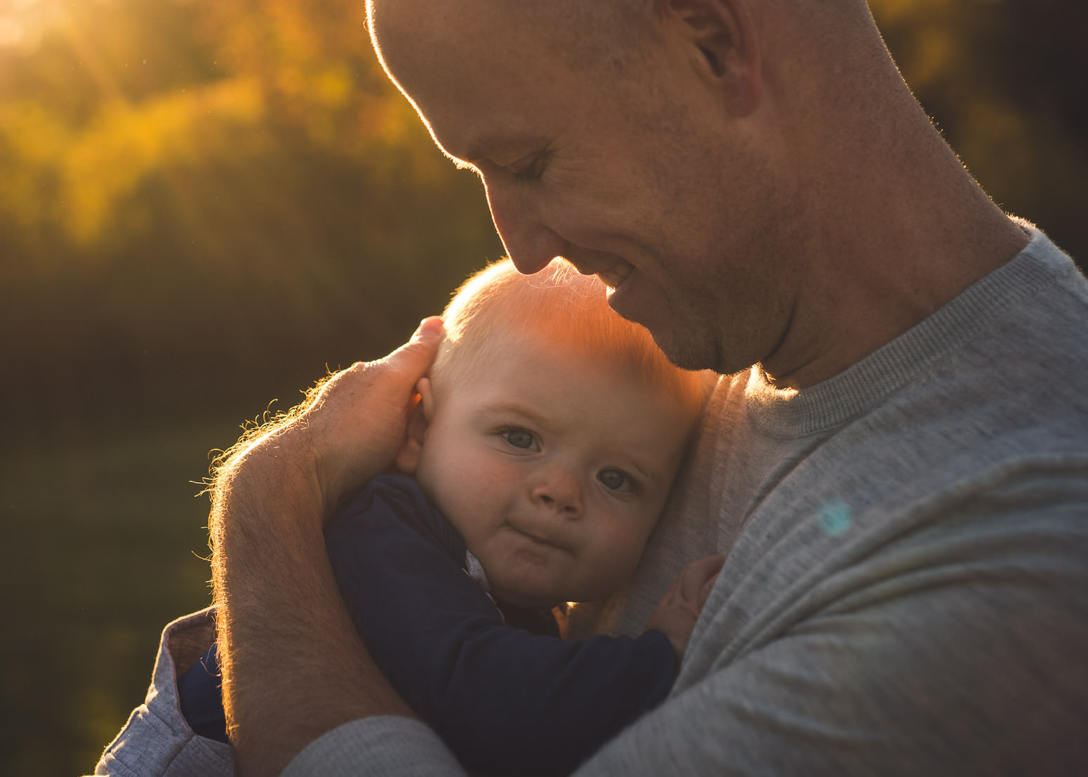 Father holds newborn son in sunlight